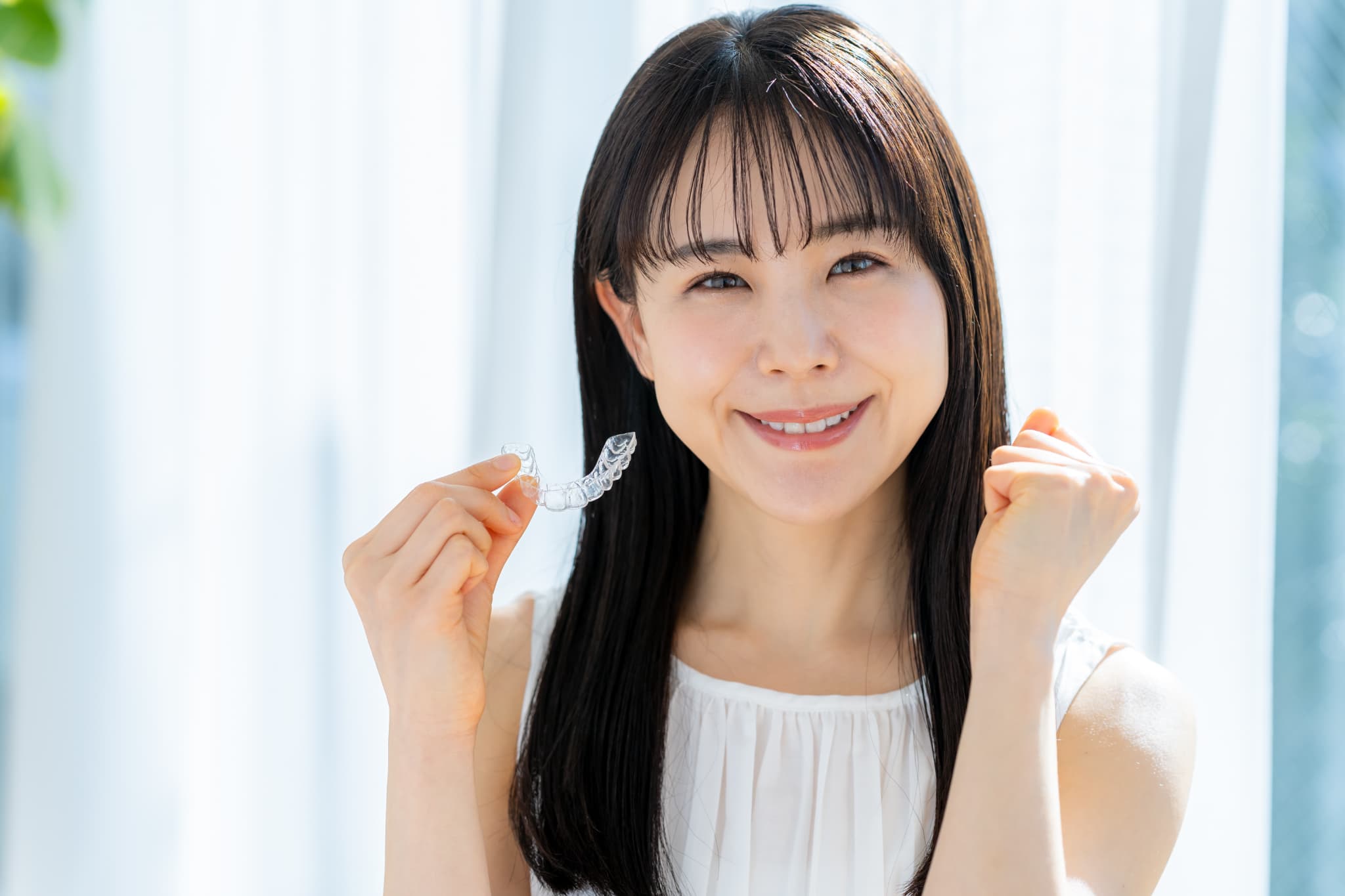 インビザラインのマウスピースを持ちガッツポーズをする女性